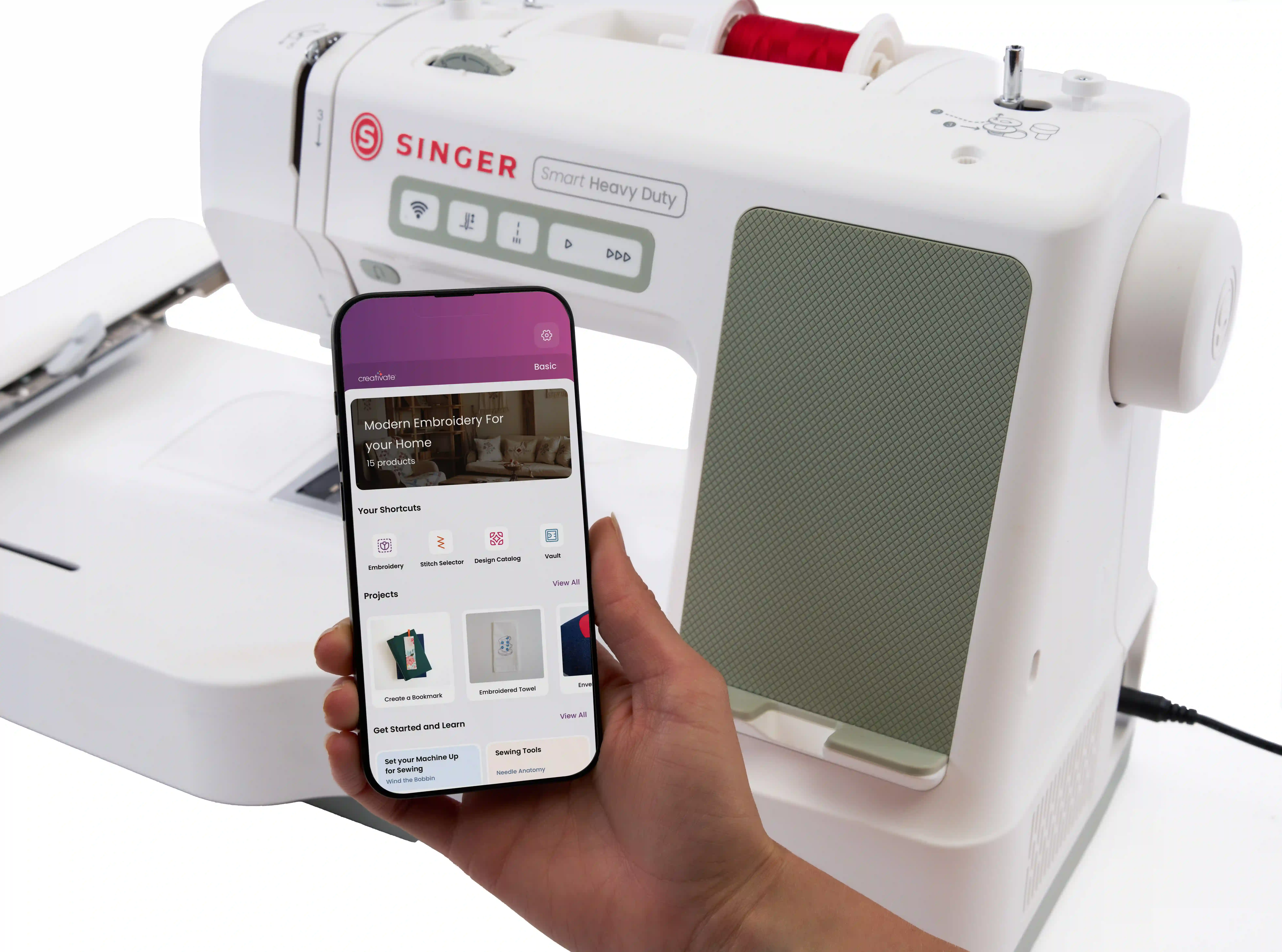 Smartphone vor der Nähmaschine mit geöffneter CREATIVATE™ App, die Stickprojekte und Anleitungen zeigt.